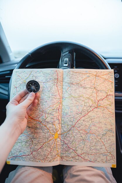 Foto close de um homem com uma bússola e um mapa nas mãos dentro de um carro