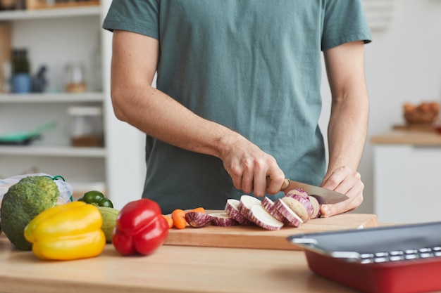 Close de um homem cortando legumes com uma faca na tábua na cozinha