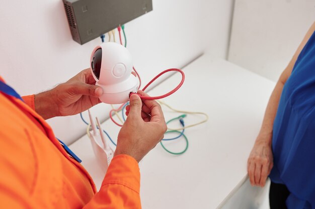 Close de um homem irreconhecível segurando uma câmera com fio e instalando em casa sob o controle do dono da casa