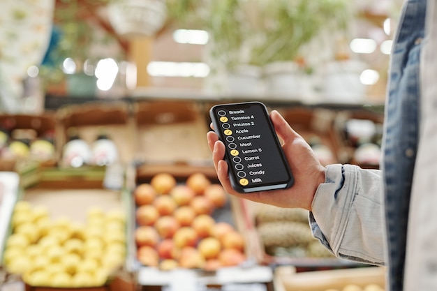 Close de um homem irreconhecível usando o aplicativo de lista de verificação enquanto compra comida no mercado de fazendeiros