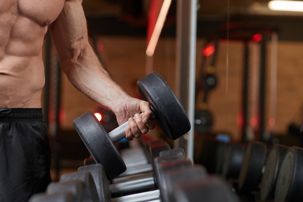 Close de um homem musculoso levantando uma barra durante o treinamento na academia