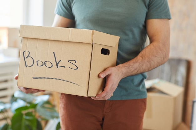 Close de um homem segurando uma caixa de papelão com livros enquanto movia a casa