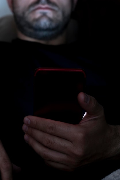 Foto close de um homem sentado no sofá à noite, fazendo uso do smartphone