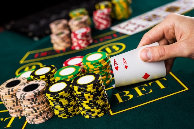 Close de um jogador de pôquer levantando as pontas de duas cartas de ases na mesa verde do cassino com ases