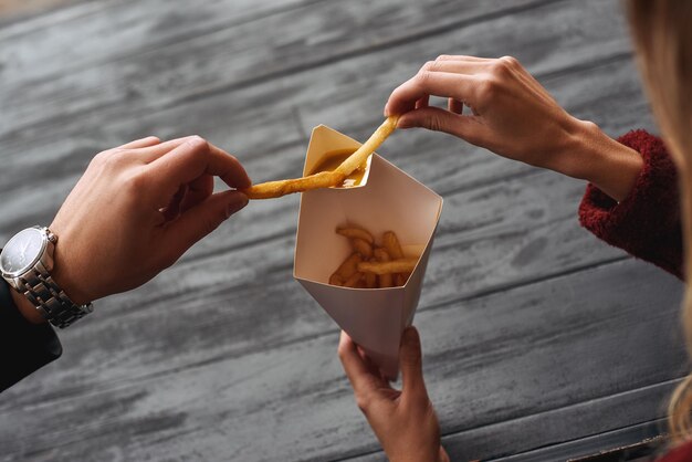 Close de um jovem casal comendo batatas fritas no mercado de comida de rua