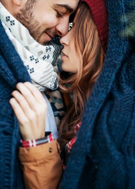 Close de um jovem casal de homem e mulher, vestindo roupas quentes, se abraçando em um dia de inverno sob um grande lenço de malha