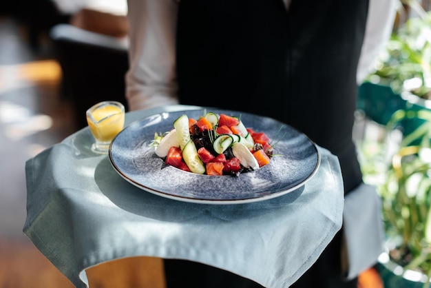 Close de um jovem garçom em um uniforme elegante carregando uma salada requintada para um cliente em um belo restaurante gourmet serviço de mesa no restaurante