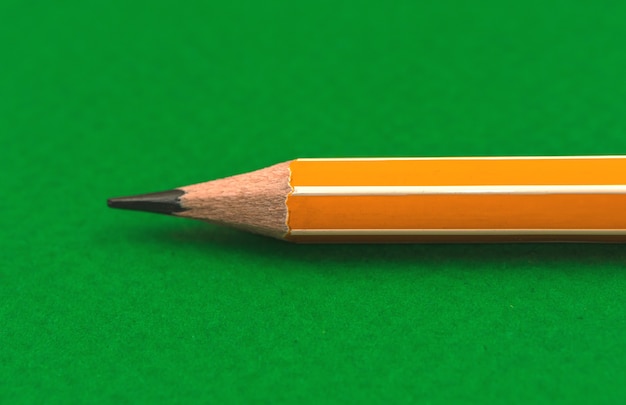 Close de um lápis escolar novo e afiado, lápis amarelo, papelaria escolar, foto de fundo verde da área de trabalho