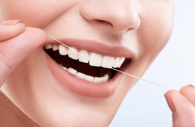 Close de um lindo sorriso branco como a neve. Dentes fortes e brancos, cuidados com os dentes. Cuidados de saúde, conceito estomatológico para dentistas. Só sorria, limpando os dentes com fio dental