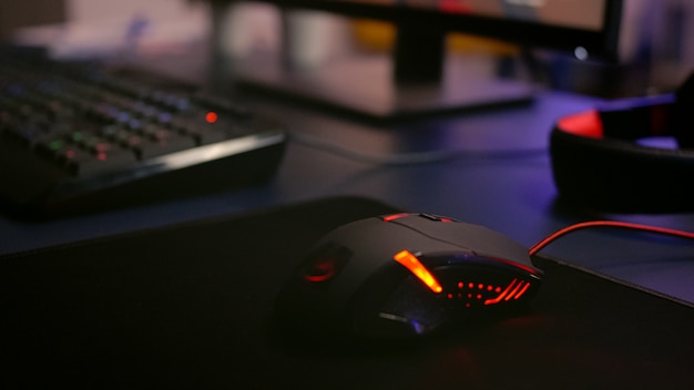 Close de um mouse profissional com iluminação RGB durante o torneio de videogame de atirador online. Estúdio doméstico de jogador de videogame esport usando um PC poderoso para jogos