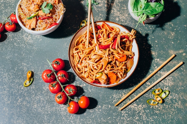 Close de um prato de macarrão chinês com carne e vegetais em pratos e pauzinhos chineses em um gramado