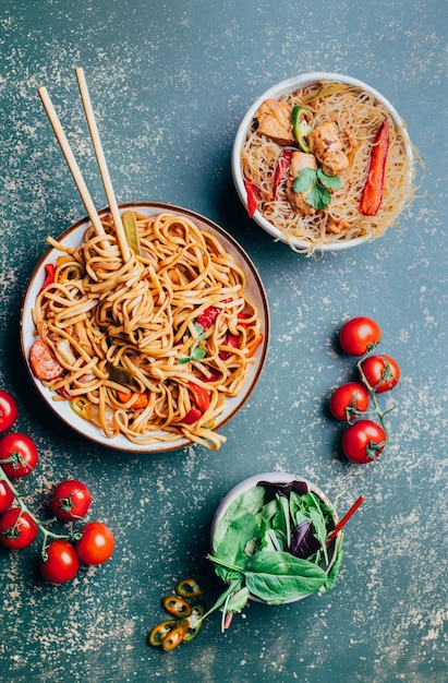 Close de um prato de macarrão chinês com carne e vegetais em pratos e pauzinhos chineses em um gramado