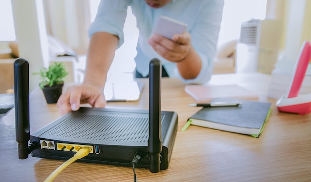 Close de um roteador sem fio e um homem usando smartphone na sala de estar em casa, equipamento para trabalhar em casa