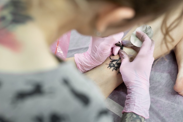 Close de um tatuador fazendo uma tatuagem na perna de uma jovem no salão