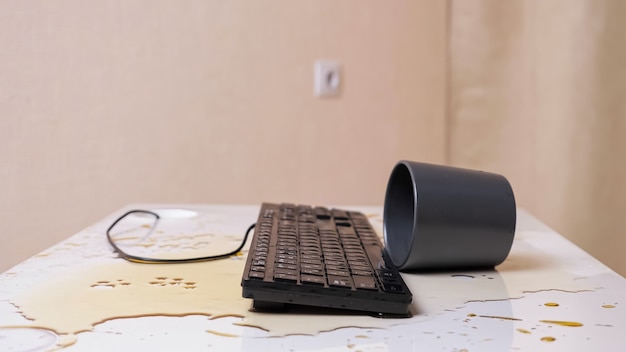 Close de um teclado encharcado de café com uma xícara virada nas proximidades, vista lateral