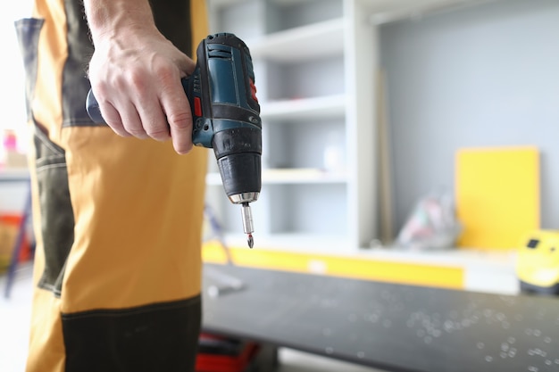 Close de um trabalhador braçal profissional vestindo uniforme brilhante e segurando uma furadeira elétrica qualificado