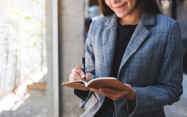 Close de uma bela empresária asiática segurando e escrevendo em um caderno