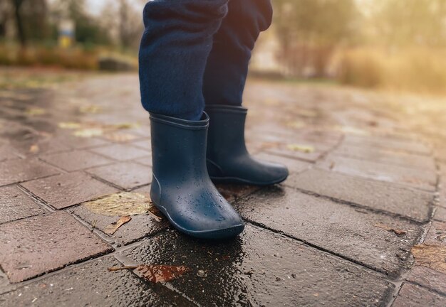 Close de uma criança com botas de borracha na calçada molhada depois da chuva