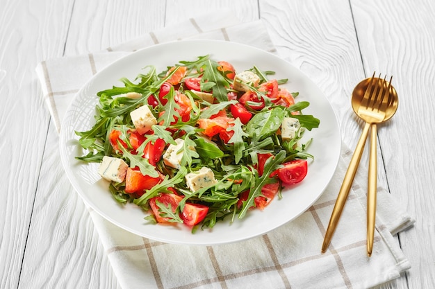 Close de uma deliciosa salada de tomate e rúcula de salmão saudável com queijo azul em um prato branco