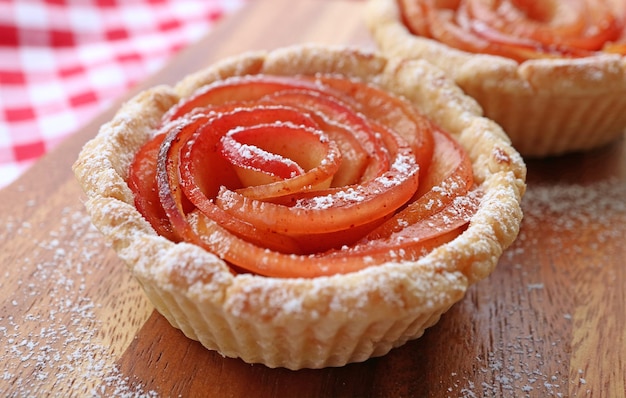 Close de uma deliciosa tartelete em forma de rosa de maçã de dar água na boca em uma tábua de pão de madeira