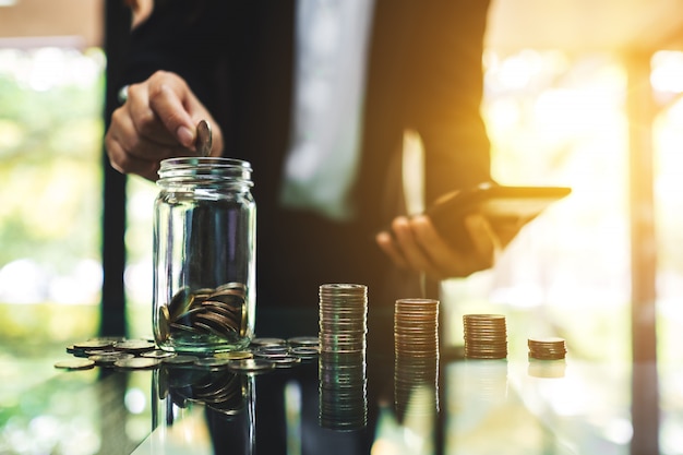 Close de uma empresária colocando moedas em uma jarra de vidro, cálculo e empilhamento de dinheiro para salvar e conceito financeiro
