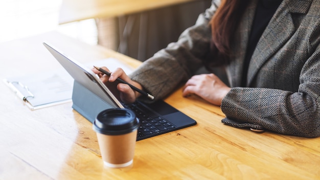 Close de uma empresária trabalhando e tocando na tela do tablet como um computador pc com xícara de café e papelada em cima da mesa