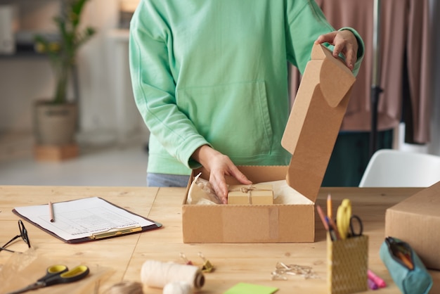 Close de uma jovem colocando um presentinho para o cliente no pacote