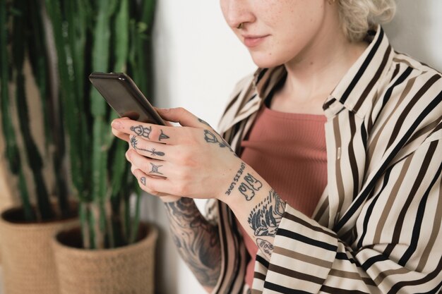 Close de uma jovem com tatuagens nas mãos, segurando um telefone celular e trabalhando online