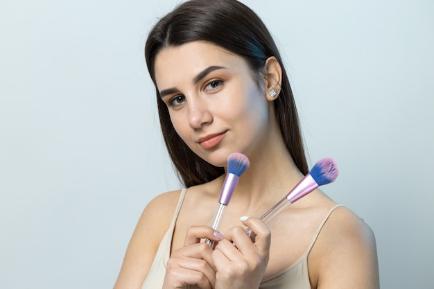 Close de uma jovem com um top claro sobre um fundo branco fazendo uma maquiagem facial