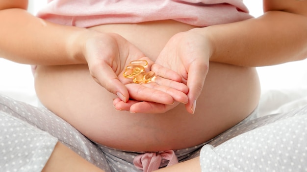 Close de uma jovem grávida abre as mãos segurando comprimidos com vitaminas