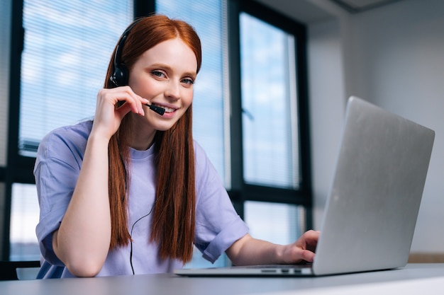 Close de uma jovem operadora usando fone de ouvido e laptop durante o atendimento ao cliente no escritório em casa