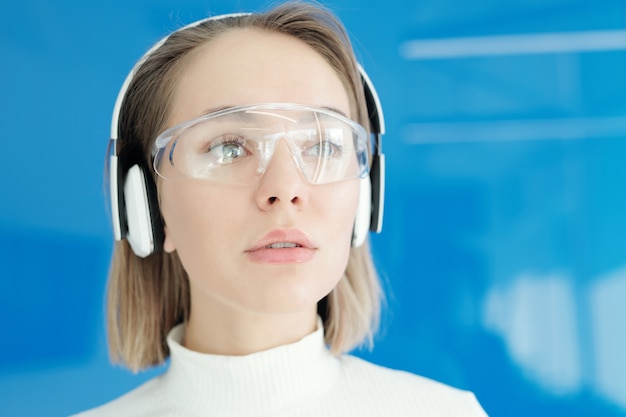 Close de uma jovem pensativa com óculos inovadores e fones de ouvido sem fio, olhando ao redor