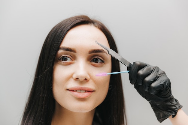 Close de uma linda garota segurando uma pinça de sobrancelha na mão perto do rosto no estúdio