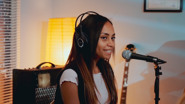 Close de uma linda garota sorridente com um fone de ouvido cantando sua música favorita no ensaio