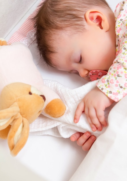 Close de uma linda menina dormindo em um berço com chupeta e brinquedo de pelúcia