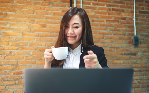 Close de uma linda mulher de negócios usando o fone de ouvido para videoconferência no computador portátil enquanto bebe café e trabalha on-line