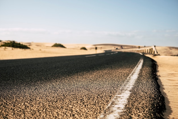 Close de uma longa estrada com dunas de areia do deserto nas laterais