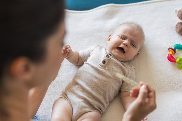 Close de uma mãe usando termômetro enquanto verifica a temperatura do bebê em casa. Foco seletivo.