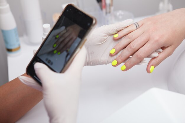 Close de uma manicure tirando fotos de unhas de clientes com seu smartphone após a manicure