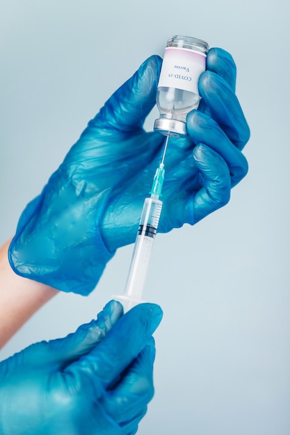 Close de uma mão em uma luva protetora azul segurando uma seringa médica e um frasco