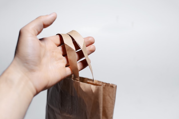 Close de uma mão masculina segurando um saco de papel ecológico na superfície branca