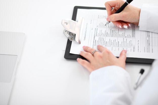 Close de uma médica preenchendo o formulário de inscrição sentado à mesa no hospital