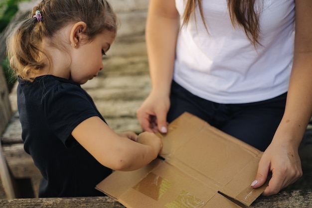 Close de uma menina com a mãe preparando papelão para reciclar o lixo doméstico, separando a família