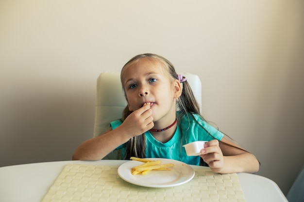 Close de uma menina comendo batatas fritas na cozinha