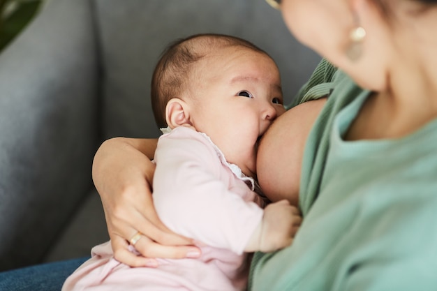 Close de uma menina comendo leite enquanto a mãe a segura nas mãos