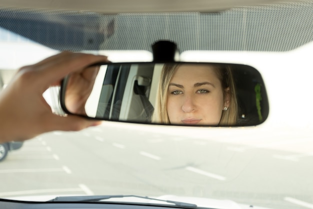 Close de uma mulher ajustando o espelho do carro e olhando no reflexo