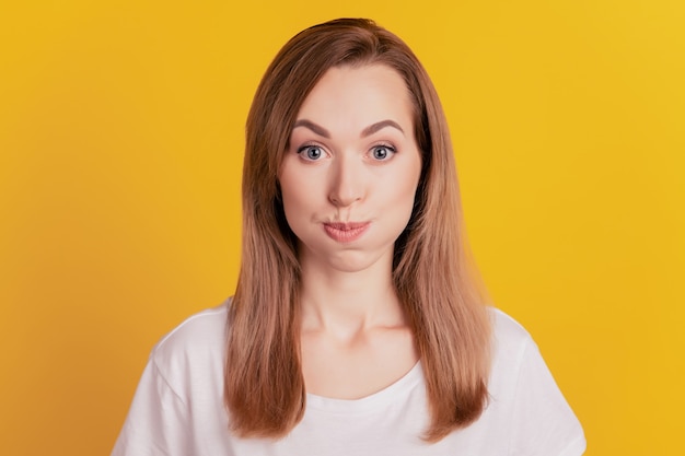 Close de uma mulher com cara engraçada, bochechas estufadas e inflar sopro de ar sobre fundo amarelo