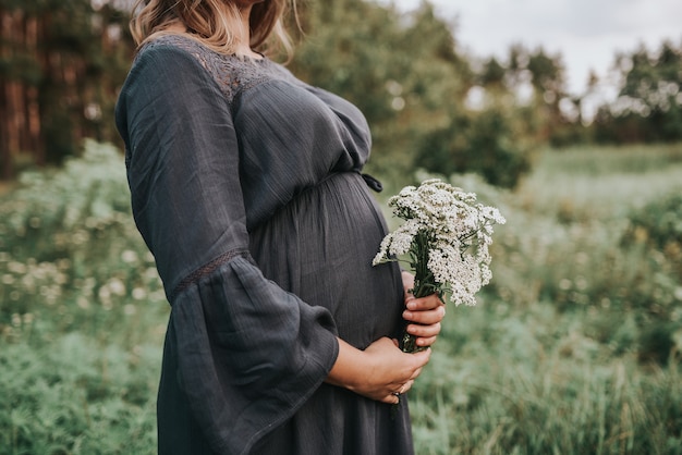 Close de uma mulher grávida com as mãos na barriga no fundo da natureza