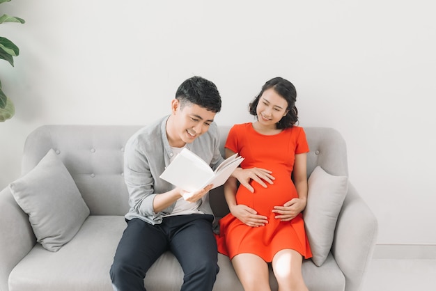 Close de uma mulher grávida e seu marido lendo um livro no sofá em casa