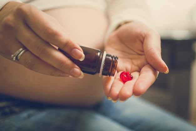 Foto close de uma mulher grávida no terceiro trimestre segurando vitaminas em pílulas